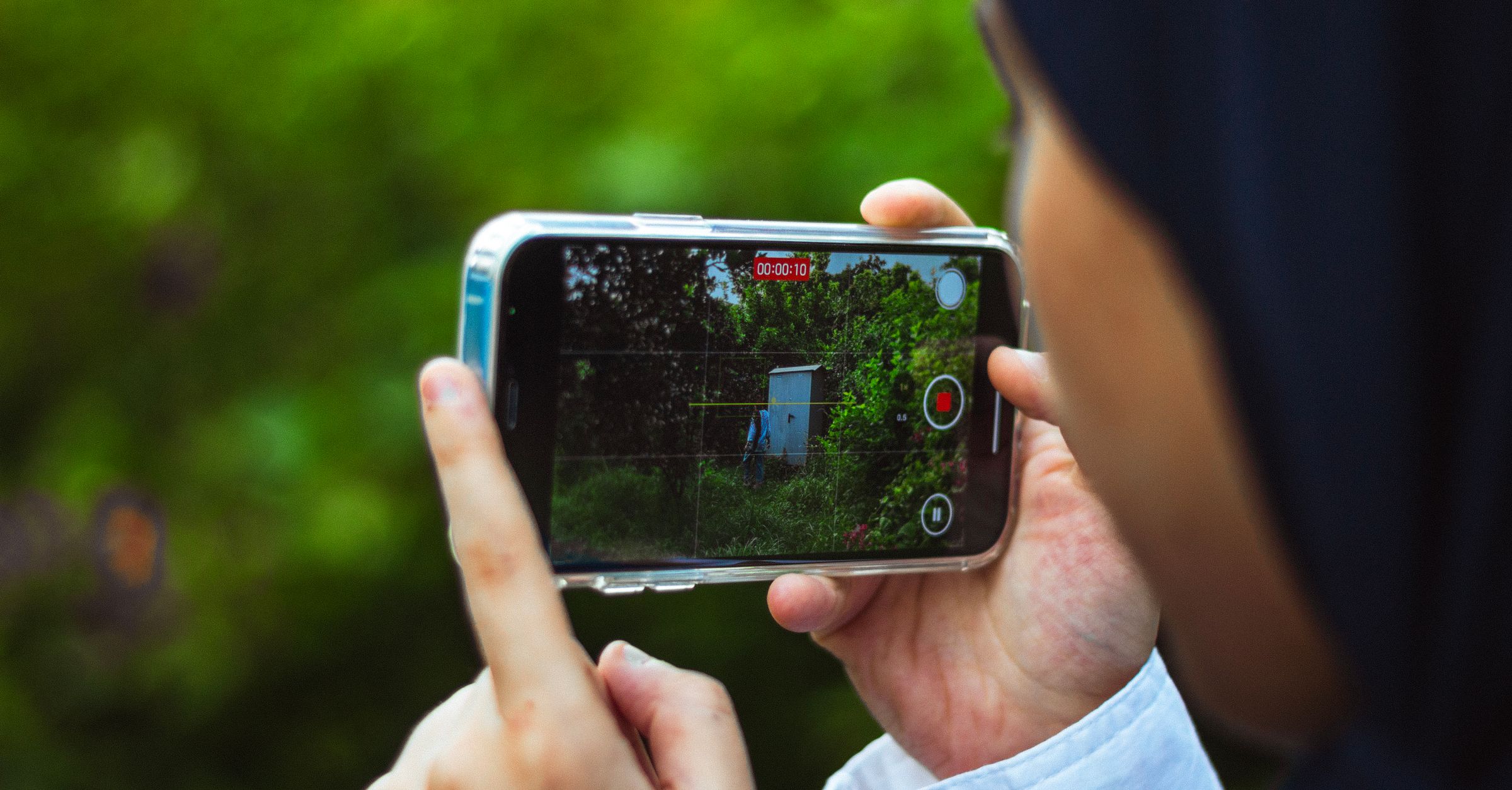 A person holding an iPhone in landscape and filming a green garden, with a recording timer on the screen