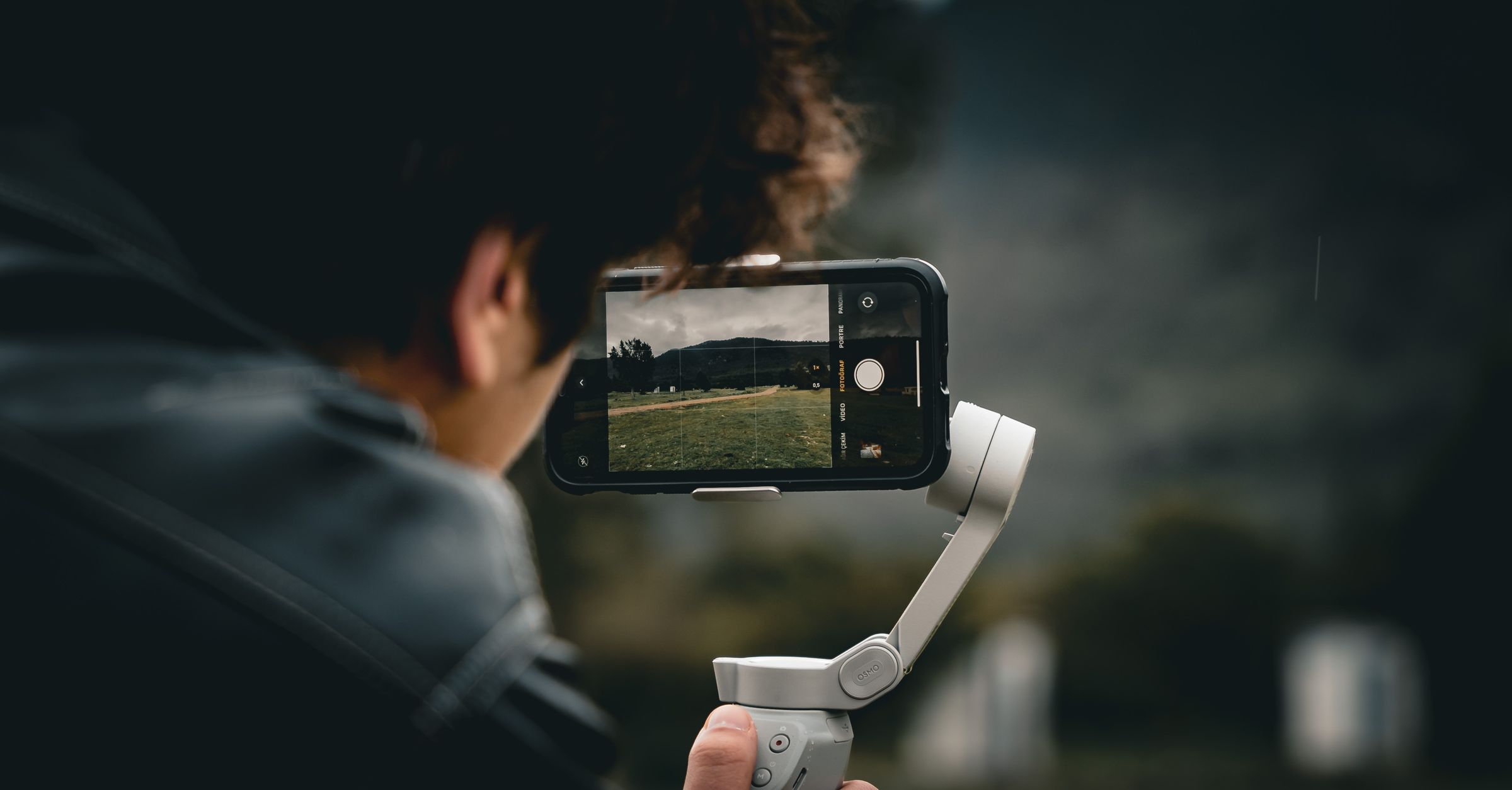 A person in a casual outfit holding a camera rig with a sea backdrop, emphasizing photography.
